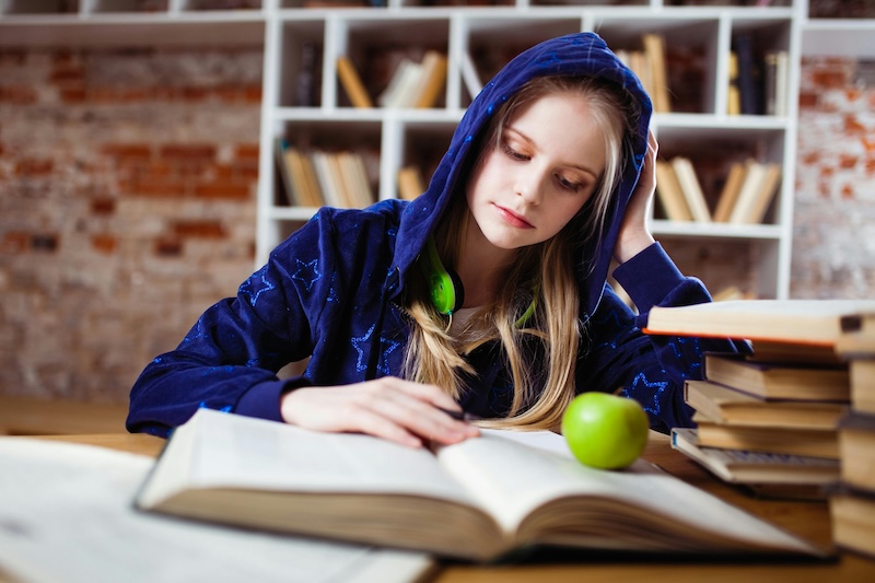 Woman wearing a blue jacket sitting on a chair near a table reading books